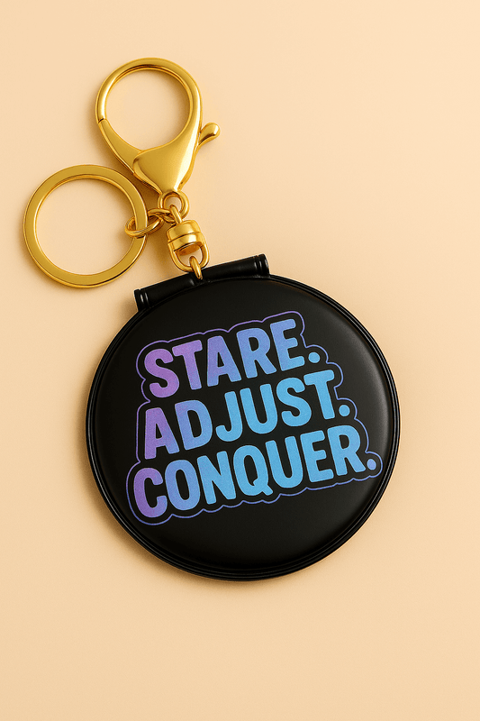 Black keychain mirror featuring the motivational phrase 'Stare. Adjust. Conquer.' with a gold clip.